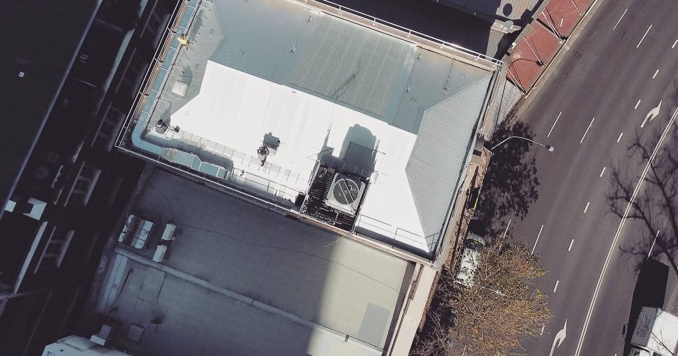 Top-down drone view of the finished metal roof on a city building beside a main road