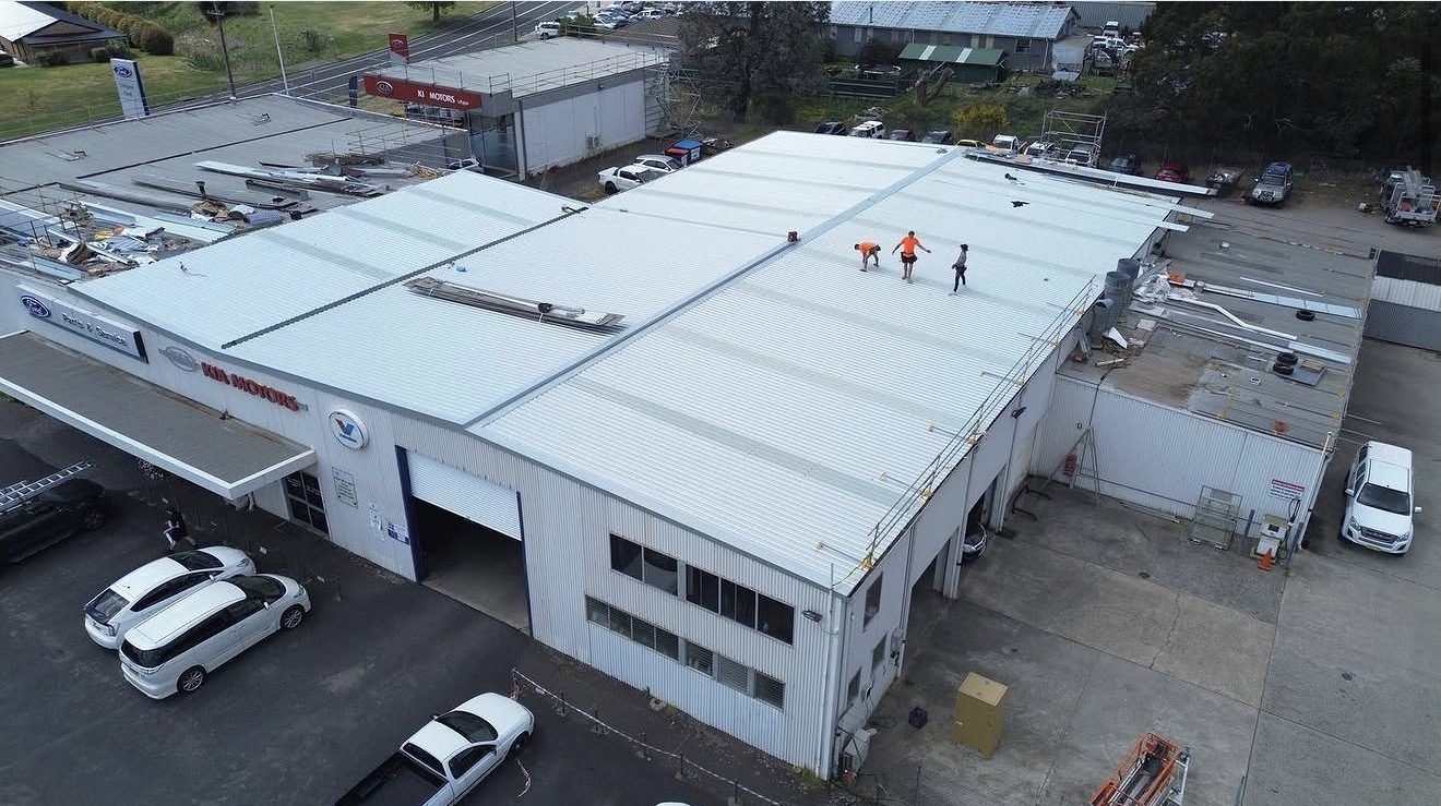 Aerial view of a car dealership with a new white metal roof and roofers on top
