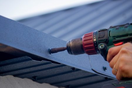 a man repairs the roof, tightens the self-tapping screw with a screwdriver